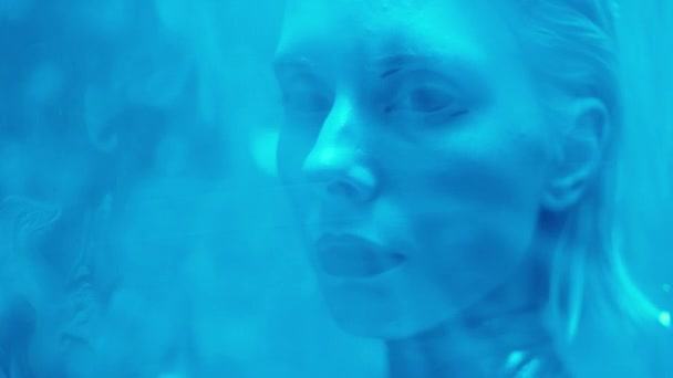 Hermosa mujer alienígena con lentes de contacto apagadas y lápiz labial oscuro posando para la cámara detrás de la luz láser azul - Metraje, vídeo