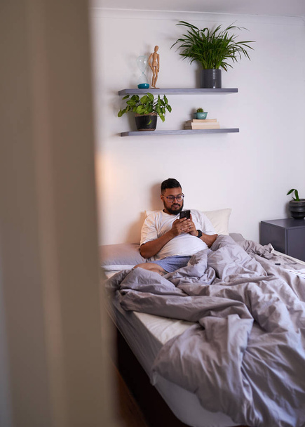 A travers la porte d'un homme paressant dans son lit sur son téléphone - Photo, image