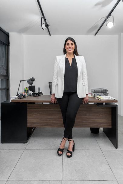 Portret van een jonge zakenvrouw die glimlacht en naar de camera kijkt en voor haar bureau staat. empowerment van vrouwen, vrouwendag. - Foto, afbeelding