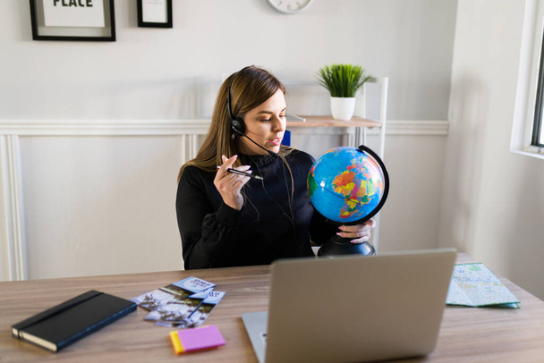 Zajęty biuro podróży z zestawu słuchawkowego trzymając globus podczas rozmowy z klientami online  - Zdjęcie, obraz
