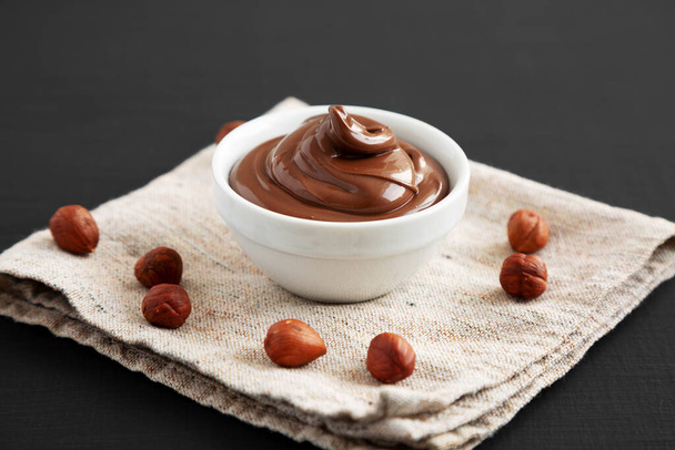 Homemade Chocolate Hazelnut Spread in a Bowl on a black background, side view.  - Photo, Image