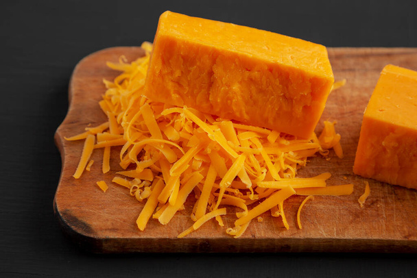 Shredded Sharp Cheddar Cheese sobre una tabla de madera rústica sobre un fondo negro, vista lateral.  - Foto, imagen