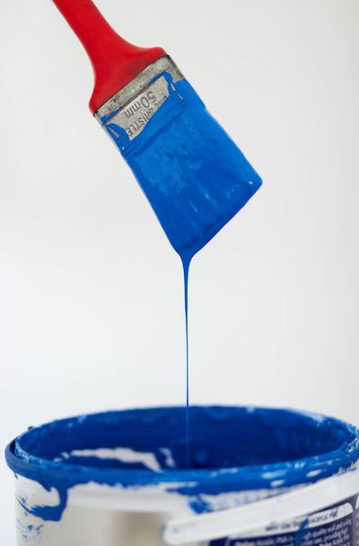 Малярський пензлик занурює блакитну фарбу. Крупним планом пензлик, що кидає синю фарбу у відро
. - Фото, зображення