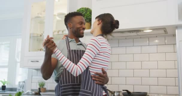 Happy diverse couple wearing blue aprons and dancing in kitchen. spending time together at home. - Footage, Video