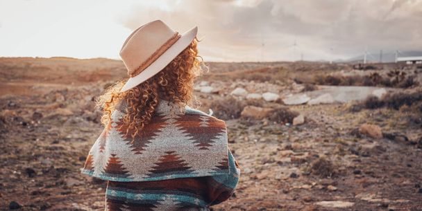 Gezgin kadın konsept yaşam tarzı, modaya uygun şapkası ve ceketi olan ve çöl manzarasında gün batımını seyreden kadın bakış açısına sahip. Gezginler ve açık hava aktiviteleri kavramı - Fotoğraf, Görsel