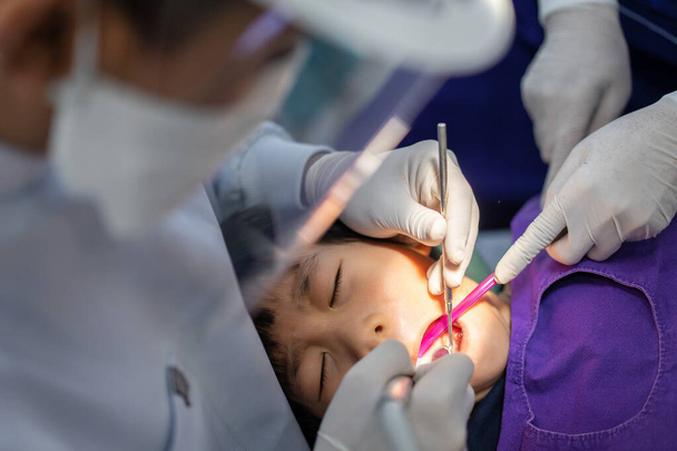 La mano del doctor dentista está trabajando en los dientes de un niño asiático de 6 años de edad paciente en una clínica dental - Foto, Imagen