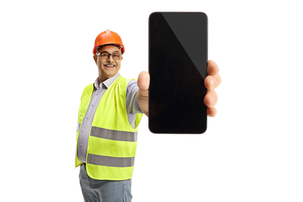 Cheerful male engineer in a reflective vest showing a smartphone isolated on white background - Foto, Bild