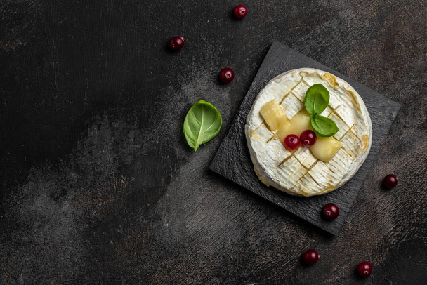 French cuisine. Baked camembert cheese with cranberries and basil leaves on a dark background, Long banner format. top view, - Foto, Imagen