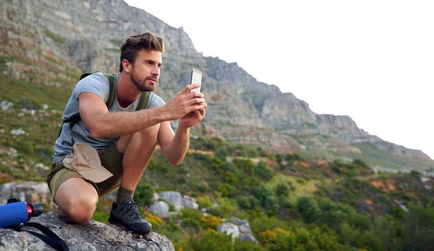Ive gotta get some pics. Shot of a handsome young man snapping pics while hiking. - Zdjęcie, obraz