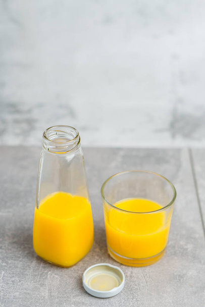 Bottle and glass with yellow liquid juice halthy beverage on gray concrete background. Orange fresh - Photo, image
