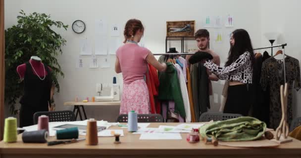 Prace projektanta mody i krawców w sklepie. Projektanci mody pracujący w swoim studio. Kolorowe tkaniny, ubrania wiszące i szyjące przedmioty są widoczne - Materiał filmowy, wideo