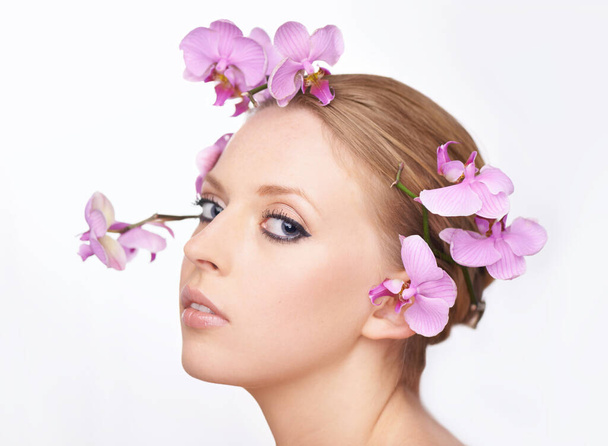 満開の若さ。彼女の髪にピンクの蘭と豪華な若い女性のスタジオ肖像画. - 写真・画像