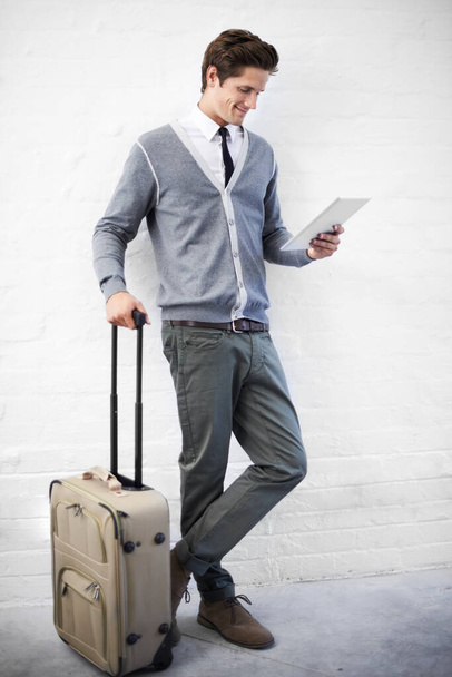Booking a flight online. A handsome young nerd with luggage working on his tablet. - Foto, immagini