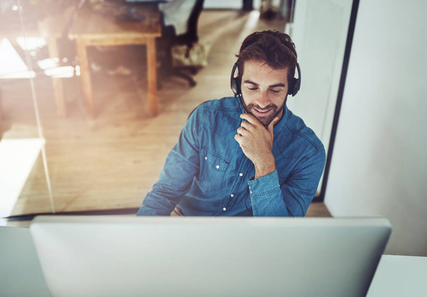 Hes always happy to be of assistance. High angle shot of a handsome young businessman wearing a headset while sitting at his desk. - Foto, Imagen