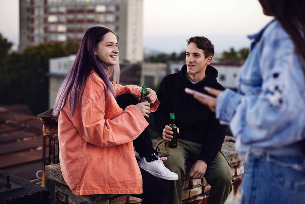 Tři dospívající přátelé sedící na střeše, chladící a pijící pivo. - Fotografie, Obrázek