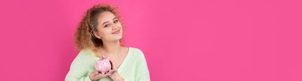 Roztomilá mladá dívka s kudrnatými zrzavými vlasy drží v rukou prasátko s růžovým selátkem. Koncept bohatství a bezpečnosti peněz. - Fotografie, Obrázek