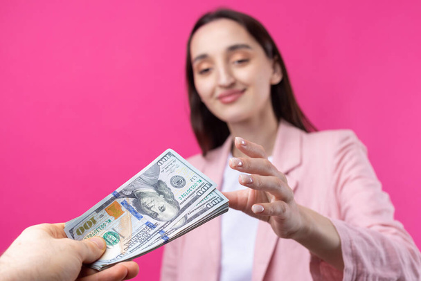 Μια γυναίκα με ροζ μπουφάν λαμβάνει δωροδοκία σε δολάρια με κόκκινο φόντο.. - Φωτογραφία, εικόνα