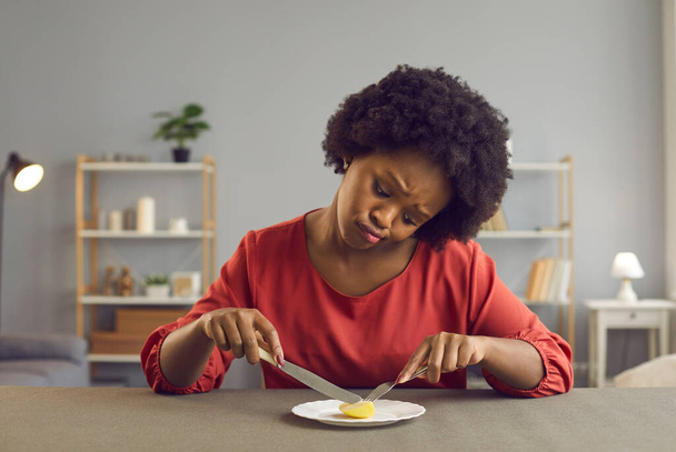 Sad african american woman frowning holding cutlery looking at apple piece - Fotoğraf, Görsel
