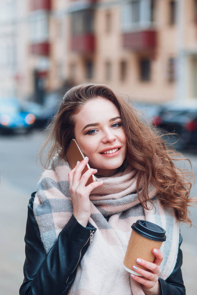 Молода жінка з кавою розмовляє на мобільному відкритому повітрі
 - Фото, зображення