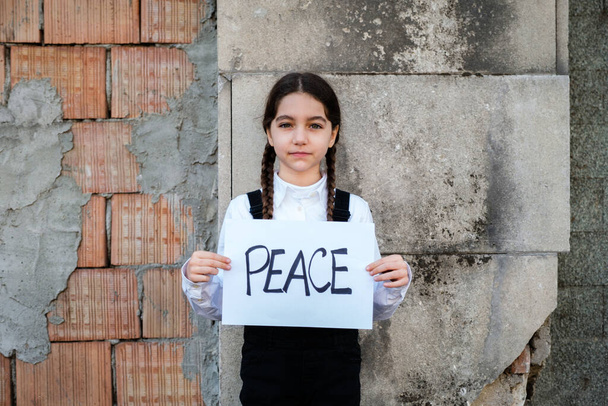 Child girl holding a poster with written PEACE in support of peace. Concept of "no war" in Ukraine and in the world. - Photo, Image