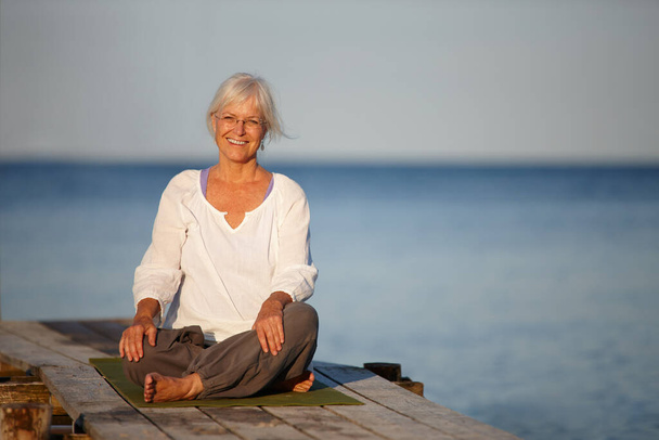 Le meilleur endroit pour le yoga. Portrait d'une jolie femme mature faisant du yoga sur une jetée sur l'océan. - Photo, image