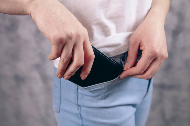 νεαρή γυναίκα βάζει το τηλέφωνο στην τσέπη σε γκρι φόντο - Φωτογραφία, εικόνα