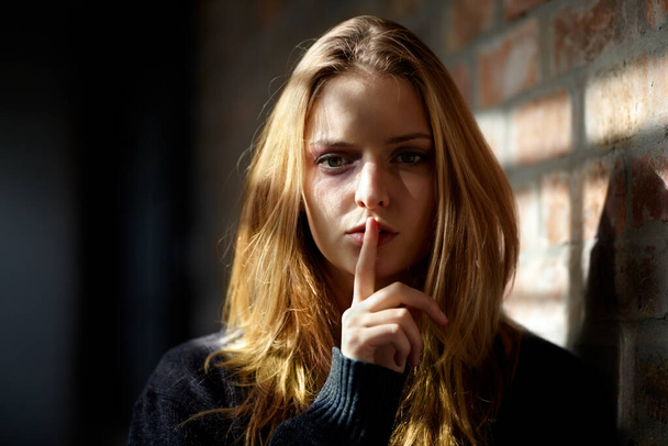 Je promets de ne rien dire... Jeune femme maltraitée faisant un geste de silence en regardant la caméra. - Photo, image