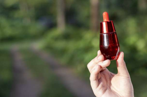 selective focus red facial serum bottle in Asian woman's hand nature background There is space for text. - Photo, Image