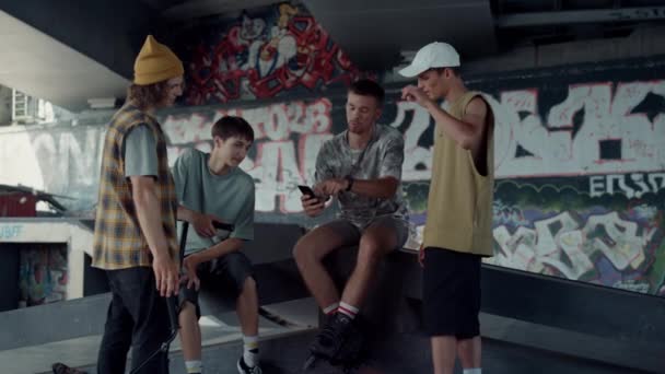 Vrolijke vrienden kijken video op mobiele telefoon op skate park met graffiti. - Video