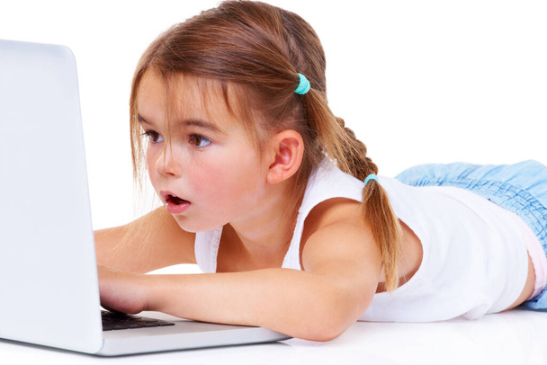 Cyberspace is a big place for a little girl. An adorable little girl looking amazed while lying down using a laptop. - Фото, изображение