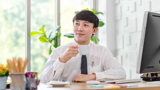 Asyalı profesyonel iş adamı resmi gömlekli, kravatlı, kahve fincanı tutan, ofisteki bilgisayar monitöründe çalışan meslektaşıyla el sallayan ve selam veren biri.. - Fotoğraf, Görsel