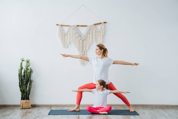 Mother and daughter stand together in second warrior pose. Yoga paired with a child. Relaxation and harmony with yourself and your body.Virabhadrasana - Foto, Bild