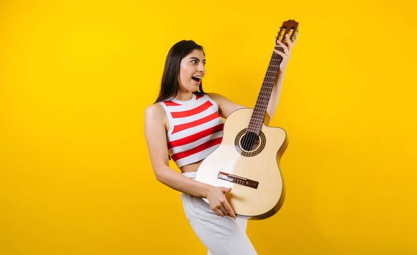 портрет молодой латинской женщины, держащей гитару на музыкальной концепции и копирующей пространство на желтом фоне в Латинской Америке - Фото, изображение