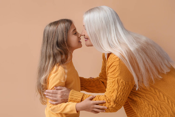 Klein meisje met haar oma aanraken neuzen op beige achtergrond - Foto, afbeelding