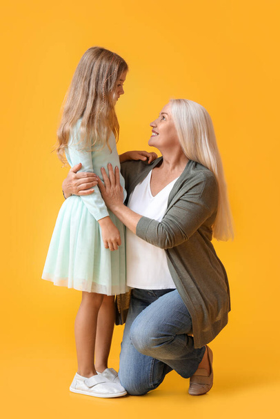 volwassen vrouw met haar kleine kleindochter op gele achtergrond - Foto, afbeelding