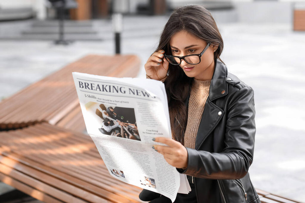 Young woman in eyeglasses reading newspaper outdoors - Foto, Imagen