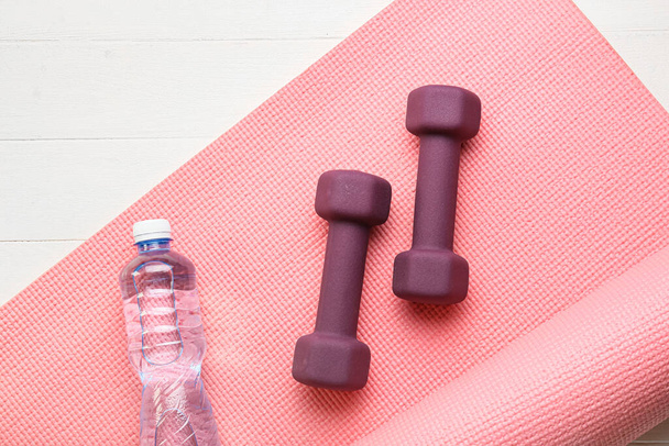 Stylish dumbbells, bottle of water and fitness mat on light wooden background - Photo, Image