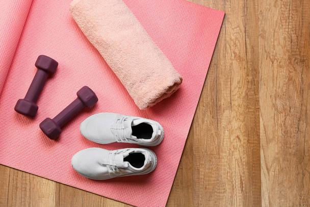 Stylové činky, ručník, fitness podložka a boty na dřevěném pozadí - Fotografie, Obrázek