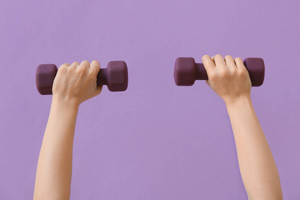 Female hands with stylish dumbbells on purple background - 写真・画像