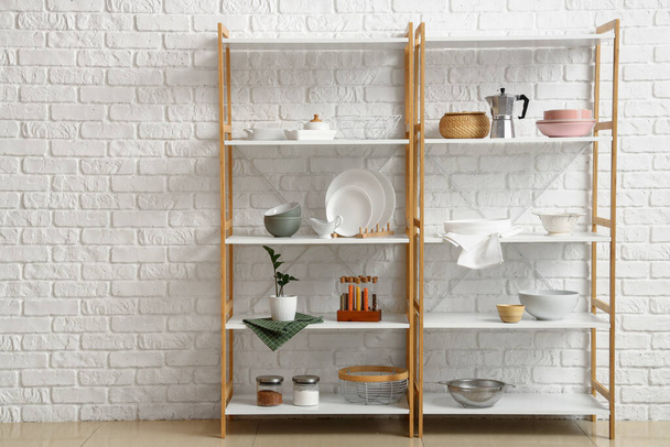 Modern shelf units with kitchenware near white brick wall - Photo, Image