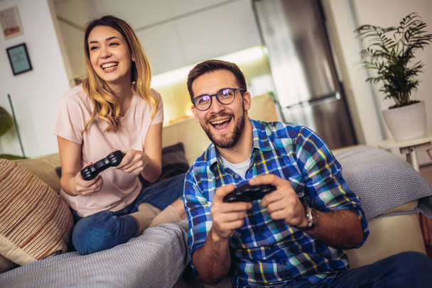 Jovem casal sentado em um sofá em uma sala de estar e jogar videogames - Foto, Imagem