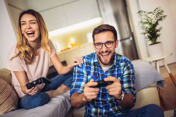 Молодая пара сидит на диване в гостиной и играет в видеоигры - Фото, изображение