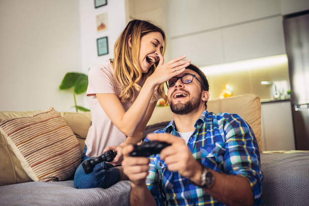 Νεαρό ζευγάρι κάθεται σε έναν καναπέ στο σαλόνι και παίζει βιντεοπαιχνίδια - Φωτογραφία, εικόνα
