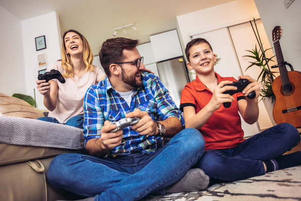 Portret szczęśliwej rodziny spędzającej wolny czas uczestnicząc w konkursie gier wideo wygrywając w nowoczesnym domu. - Zdjęcie, obraz
