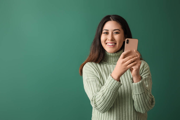 Красивая молодая азиатка с мобильным телефоном на зеленом фоне - Фото, изображение