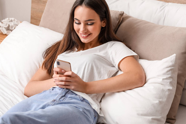 Счастливая девушка с мобильным телефоном в спальне - Фото, изображение