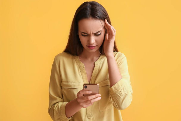 Нещасна молода жінка з мобільним телефоном на жовтому фоні
 - Фото, зображення