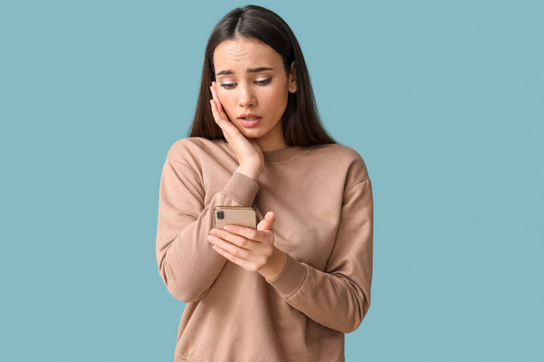 Грустная молодая женщина с мобильным телефоном на синем фоне - Фото, изображение