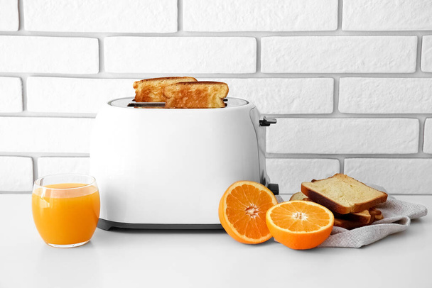 Modern toaster with bread slices and glass of orange juice on light table - Фото, зображення