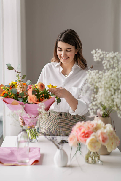 happy woman arranging flowers in vase at home - Фото, зображення